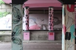 Painted columns with various artistic designs, including feathers and abstract faces. Murals in the background display stylized portraits with vibrant colors, adding an urban and creative atmosphere.
