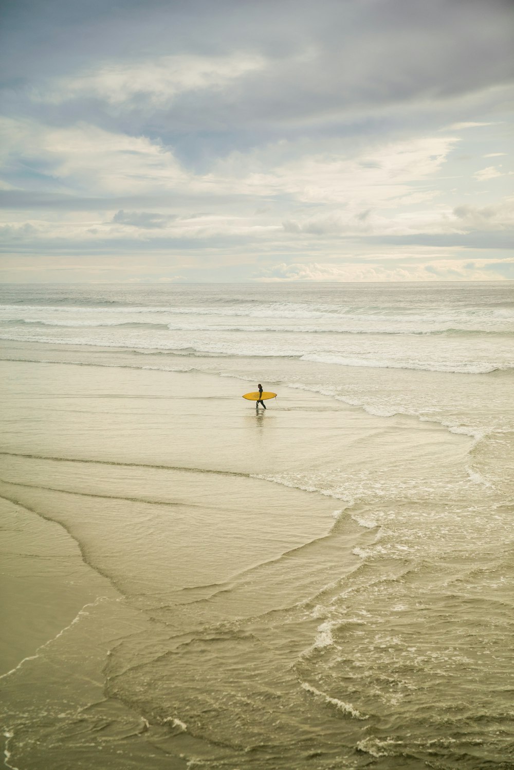 person holding yellow surfboard on seashore during daytime