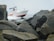 A rescue boat from a fire department is navigating through a rocky sea area with visible splashes of water. It is surrounded by large boulders along a coastline under a cloudy sky.