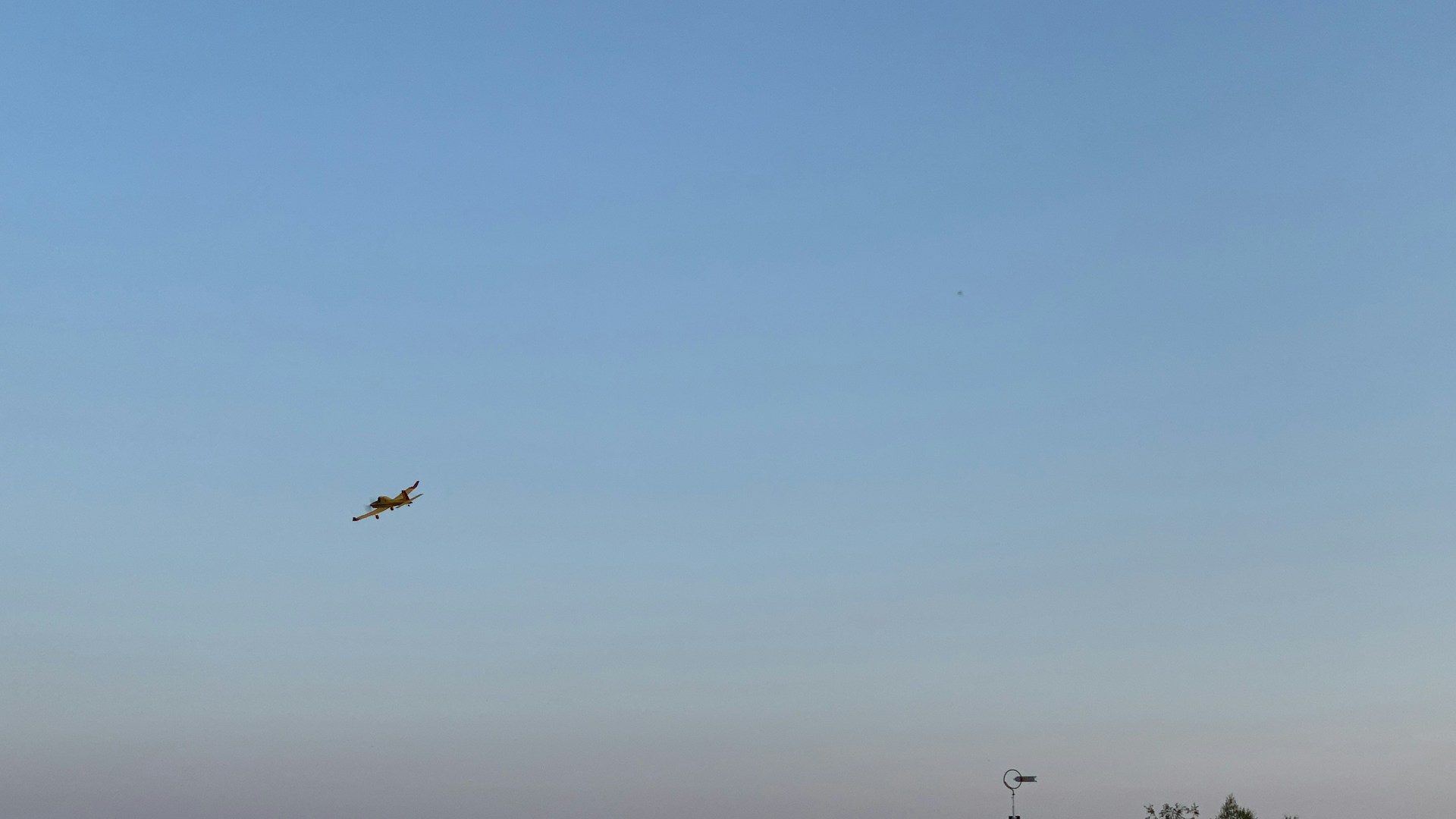 A serene ultralight aircraft soaring gently above a patchwork of green fields under a clear blue sky.