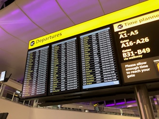 An airport departure board displays a list of flights, departure times, and gate information. The board is electronic, with a yellow header indicating 'Departures'. Another section advises passengers to allow enough time to reach their gate, along with details about gate numbers.