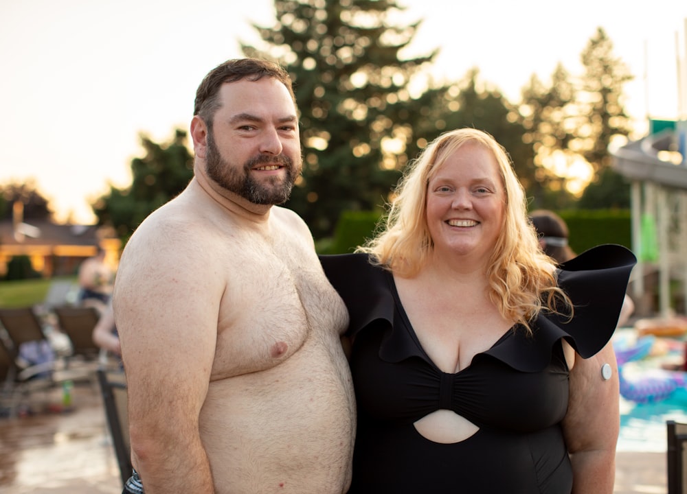 smiling topless man standing beside woman wearing black dress taking selfie