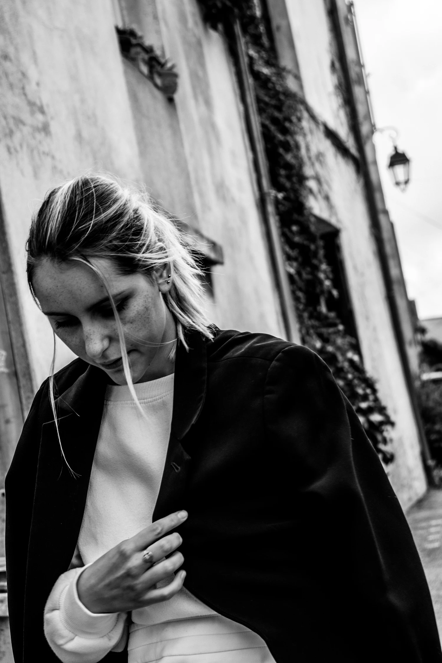 A woman in a long black coat pausing against a weathered street wall