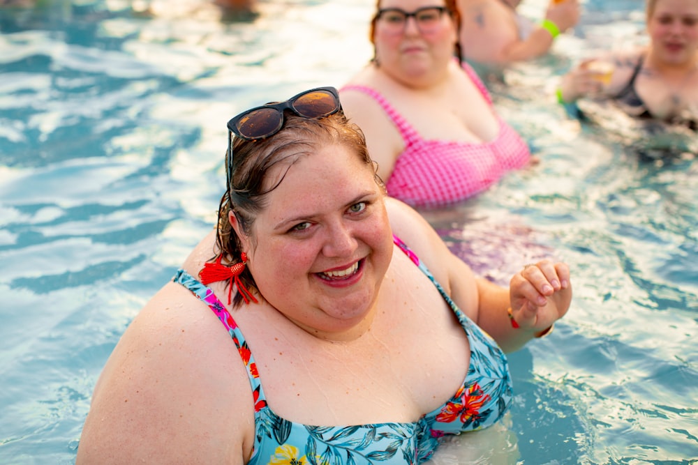 Frau trägt blaues Bikinioberteil neben Frau mit rosa Bikinioberteil, die im Wasser schwimmt