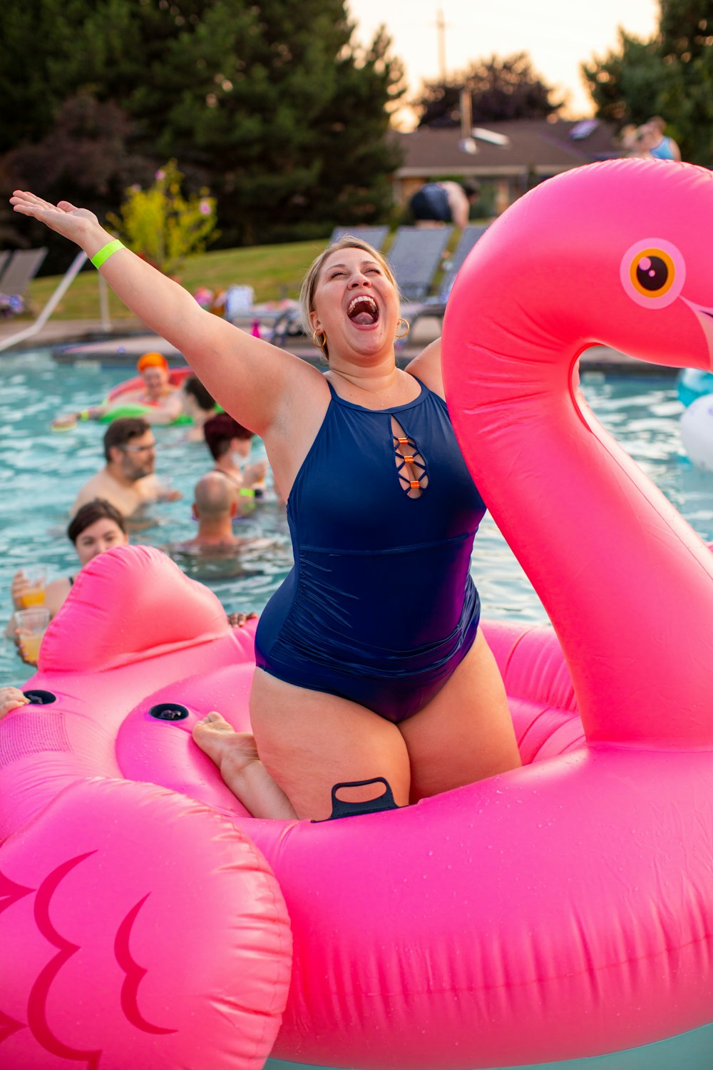 woman wearing blue swimsuit knee on pink flamingo floaters during daytime