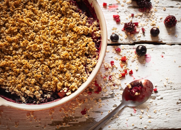 Close-up of a freshly baked crumble with golden crust and juicy fruit filling on a rustic wooden table.