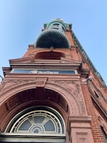 A tall brick building with intricate architectural details and engravings, featuring a prominent archway and a decorative copper element above. The building has a classical design with ornate carvings on the façade. A sign reading 'SunTrust' is visible, indicating a financial institution.