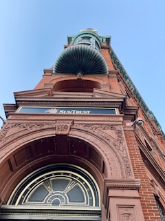 A tall brick building with intricate architectural details and engravings, featuring a prominent archway and a decorative copper element above. The building has a classical design with ornate carvings on the façade. A sign reading 'SunTrust' is visible, indicating a financial institution.