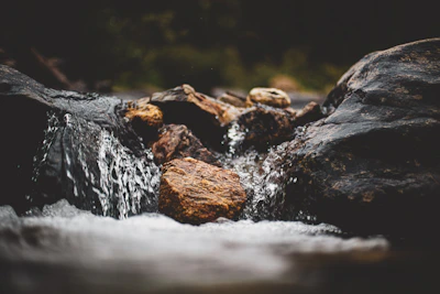Close-up of crystal-clear water droplets flowing over smooth river stones in a natural spring.