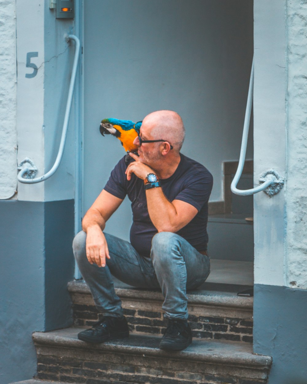 man in eyeglasses sitting on doorway