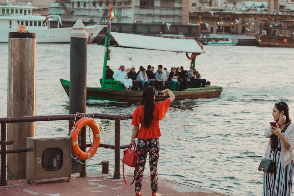 Mujer con blusa roja y pantalones florales sosteniendo una bolsa de dos vías en el muelle