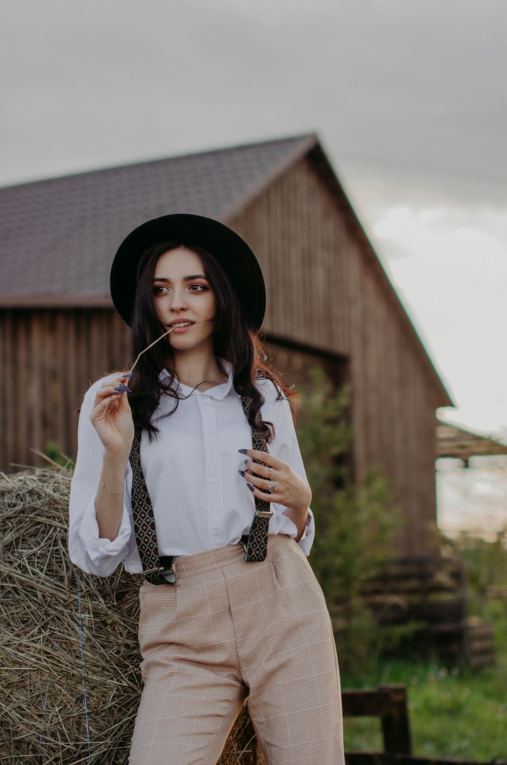 woman in white long-sleeved shirt, brown pants, black hat, and black suspenders