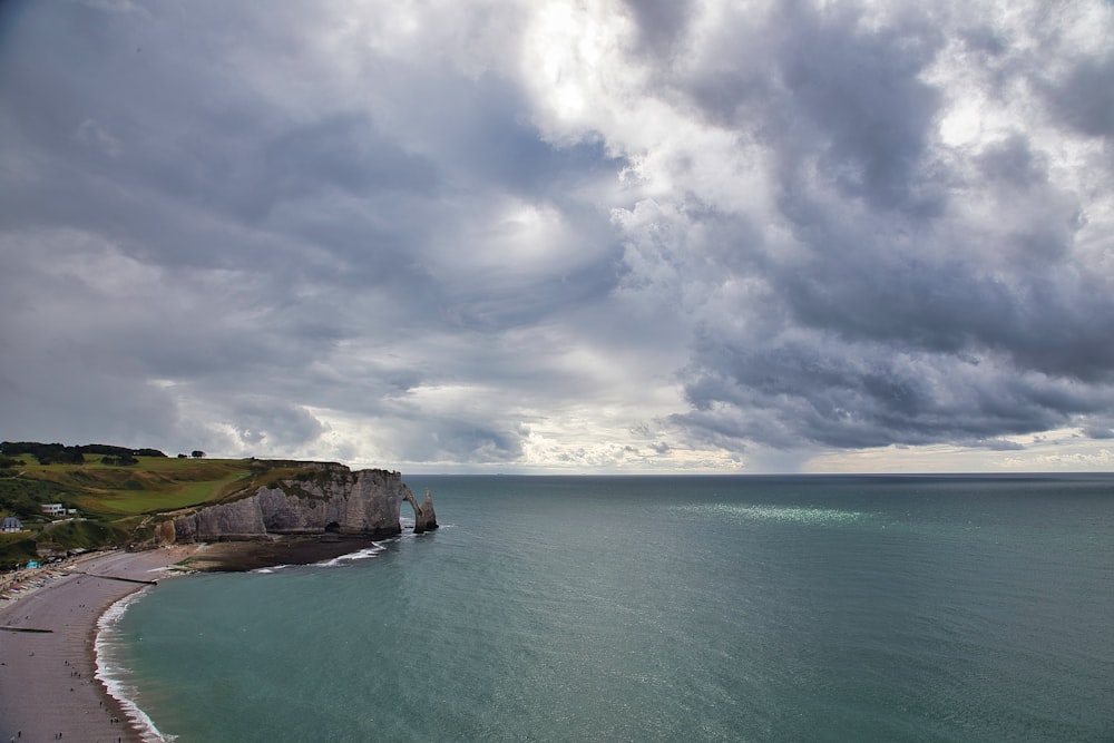 grass on cliff beside sea water under cloudy sky