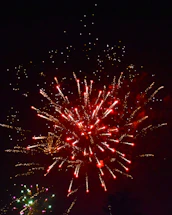 A warm, festive event scene with golden lights and fireworks glowing in the night sky.