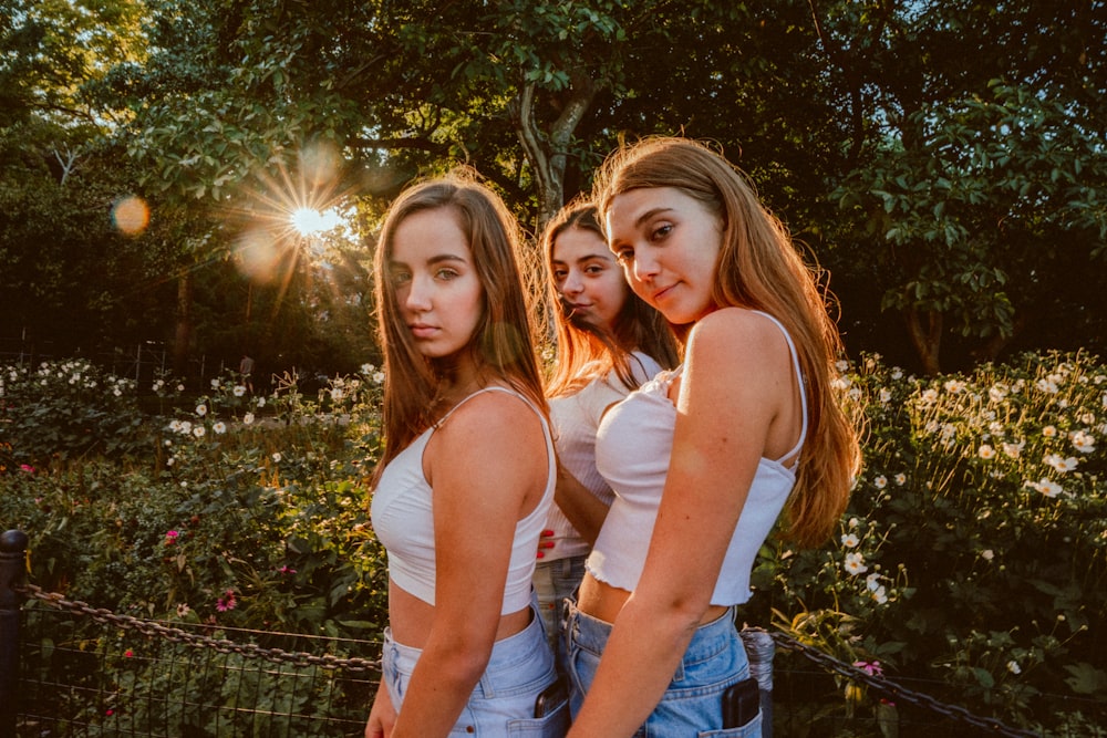 three women standing beside white-petaled flowers