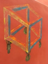 A geometric cube with transparent edges is depicted on a red background. The cube has a three-dimensional appearance and is attached to four antique-style caster wheels. The edges of the cube are colored in a spectrum of blues, yellows, and reds, giving it a vibrant and dynamic look.
