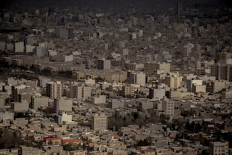 An expansive urban landscape filled with numerous high-rise buildings and apartment blocks. The densely packed architecture suggests a sprawling city scene. The buildings vary in color but mostly consist of beige, gray, and white tones, with some patches of red rooftops.