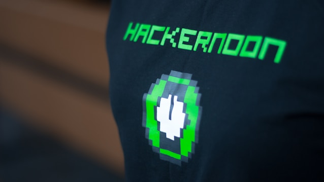 A black shirt features pixelated green text reading 'HACKERNOON' above a pixel art design of a green and white plug icon.