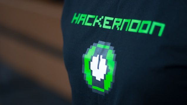 A black shirt features pixelated green text reading 'HACKERNOON' above a pixel art design of a green and white plug icon.
