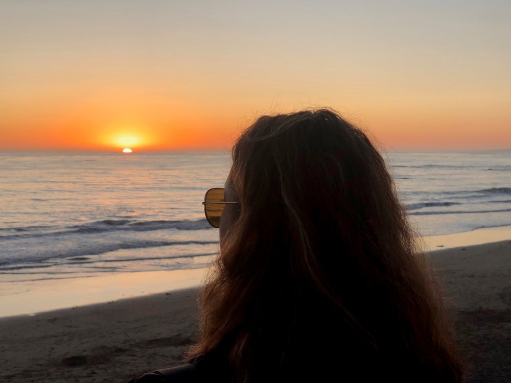 photo of woman wearing brown sunglass looking at sunset during sunset