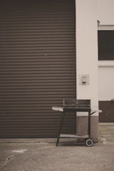 A sturdy grill cart with shelves holding spices and tools by a cozy patio.