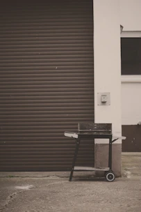 A sturdy grill cart with shelves holding spices and tools by a cozy patio.