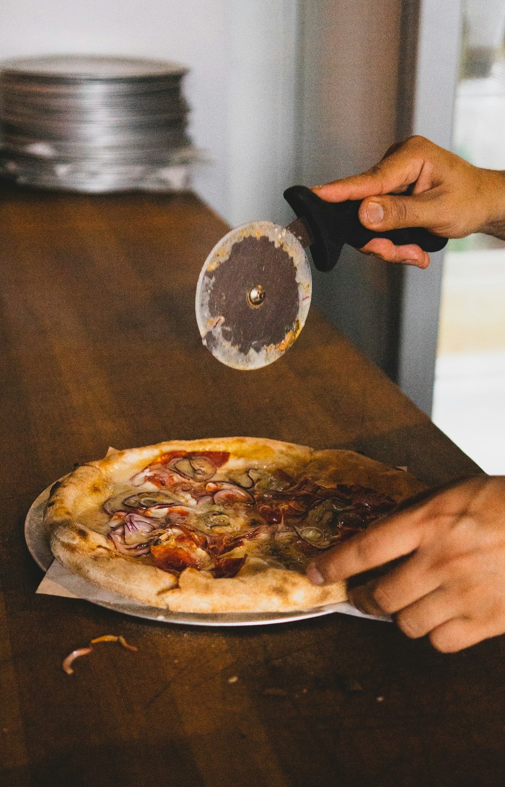 personne tenant une trancheuse à pizza au-dessus d’une pizza