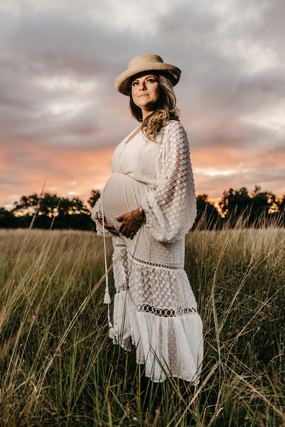 a pregnant woman standing in a field at sunset