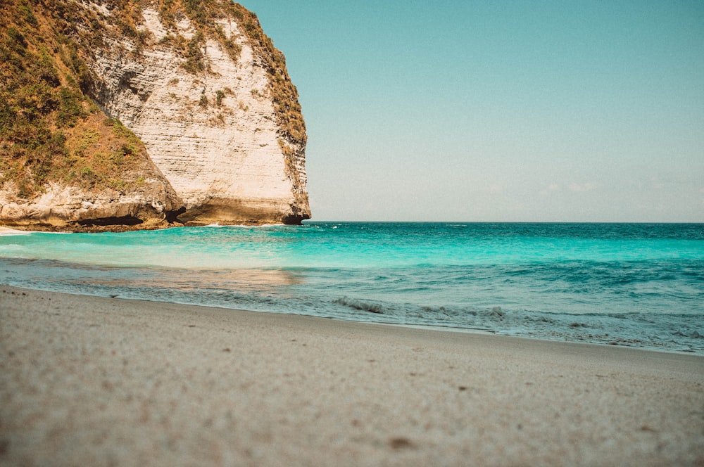 a sandy beach next to the ocean with a cliff in the background