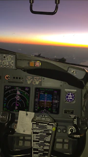 Close-up of a flight simulator setup with screens showing a detailed runway approach at sunset.