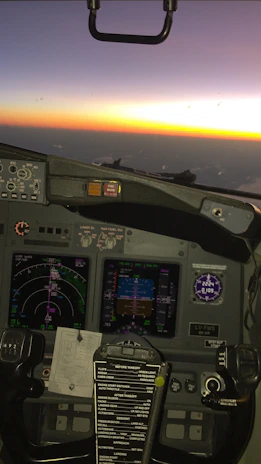 Close-up of a flight simulator setup with screens showing a detailed runway approach at sunset.