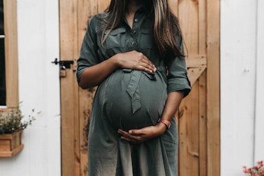 pregnant woman in green dress near door lovingly supporting her abdomen