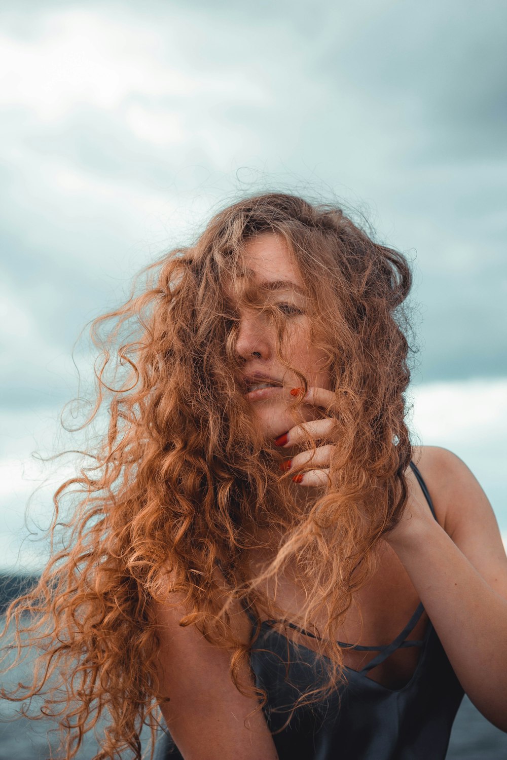 a woman with red curly hair standing on the beach