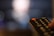A close-up of a television remote control, primarily dark in color with a prominent red power button. The background is blurred, suggesting a focus on the remote.