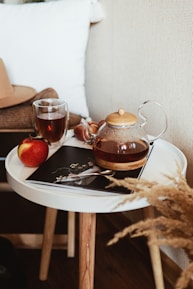 teapot near gray stainless steel teaspoon, red apple fruit, and clear glass mug on round white wooden end table