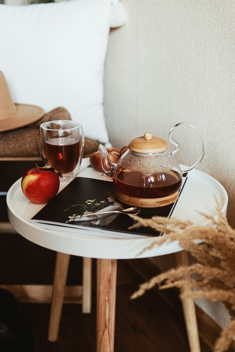teapot near gray stainless steel teaspoon, red apple fruit, and clear glass mug on round white wooden end table