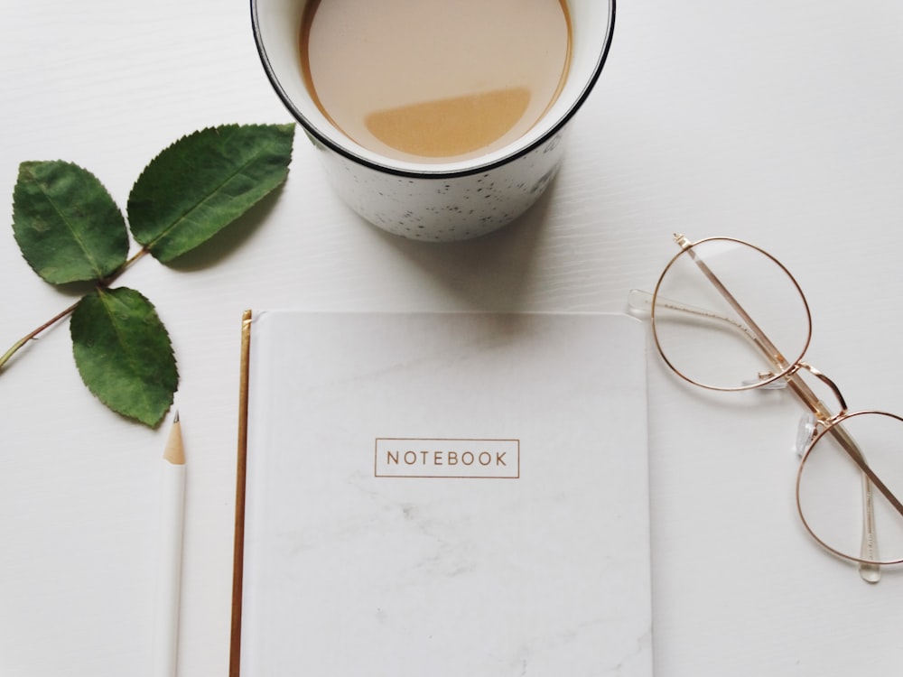 gold framed eyeglasses beside cup and notebook