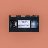 A VHS cassette labeled 'A Beautiful Mind' is centrally placed against a muted pink background, emphasizing the retro aesthetic of the object.