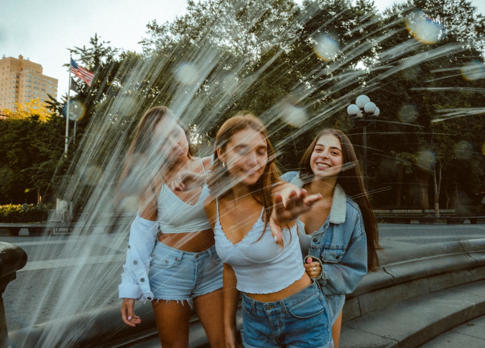 three women standing near sprinkling water