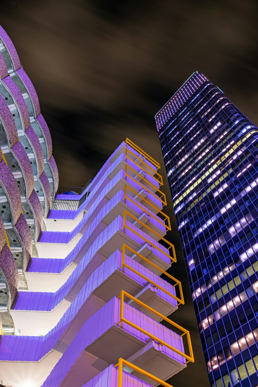 low-angle photography of white concrete building and curtain wall high rise building at night