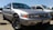 A silver Honda sedan with a classic design is parked outdoors, with other cars visible in the background. The car's body is shiny and the wheels have detailed rims.