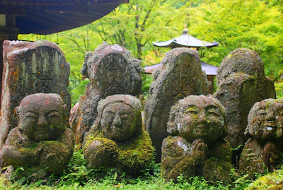 Ancient stone statues partially covered in moss, nestled in a quiet garden.