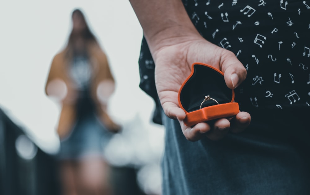 shallow focus photography unknown person holding silver-colored ring in box