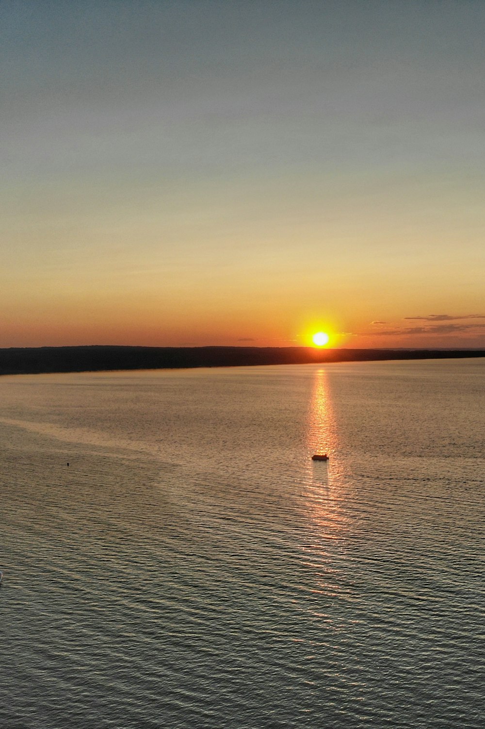 the sun is setting over the ocean with a boat in the water