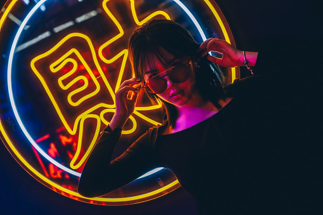 woman touching the temples of her sunglasses in front of neon signage