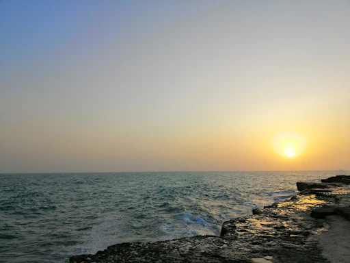 A serene coastal sunset with gentle waves meeting a rocky shore under a deep blue sky.