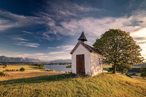 A rustic chapel surrounded by fields at sunset.