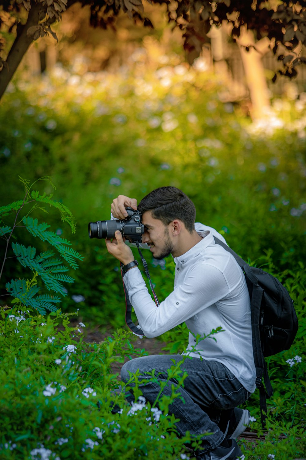 hombre con mochila negra sentado y tomando foto en los árboles