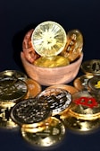 A wooden bowl filled with various golden and copper-colored cryptocurrency coins is surrounded by more coins on a dark surface. Each coin features distinct cryptocurrency symbols, including Bitcoin, Ethereum, and others.