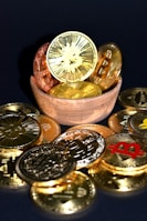 A wooden bowl filled with various golden and copper-colored cryptocurrency coins is surrounded by more coins on a dark surface. Each coin features distinct cryptocurrency symbols, including Bitcoin, Ethereum, and others.